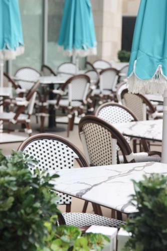 Outdoor patio seating with dark brown and white rattan chairs sit 4 to a table underneath large umbrellas.